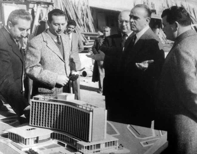 Ο τότε πρωθυπουργός Κωνσταντίνος Καραμανλής εξετάζει τη μακέτα του ξενοδοχείου. Μαζί του είναι ο μετέπειτα Πρόεδρος της Δημοκρατίας Κωνσταντίνος Τσάτσος, ο τότε Υπουργός Εμμανουήλ Κεφαλογιάννης και οι αρχιτέκτονες Αντώνης Γεωργιάδης και Σπύρος Στάικος- 1959